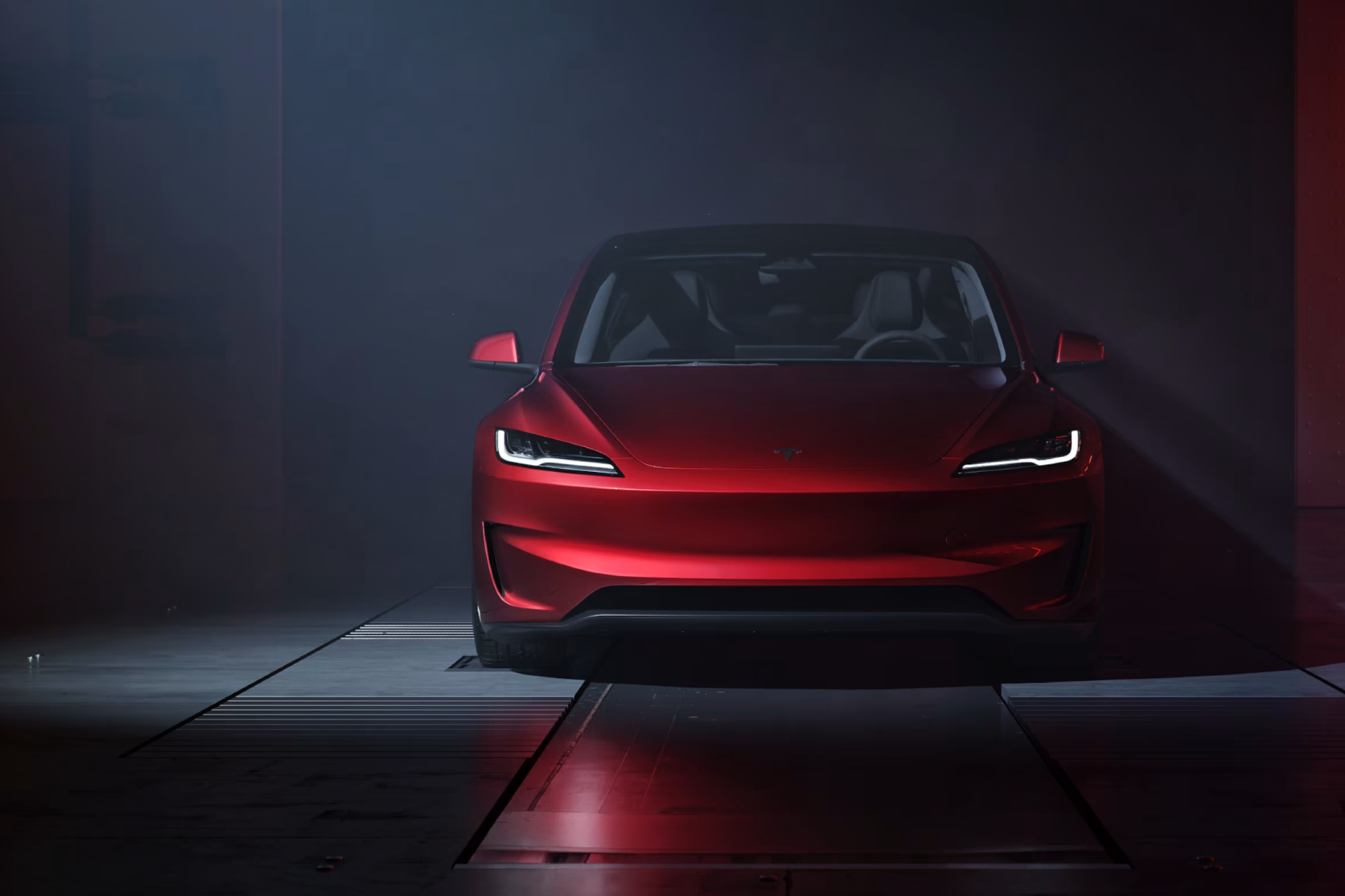 Red Tesla Model 3 Performance facing straight on parked on dark metal plates with a dark wall in the background.