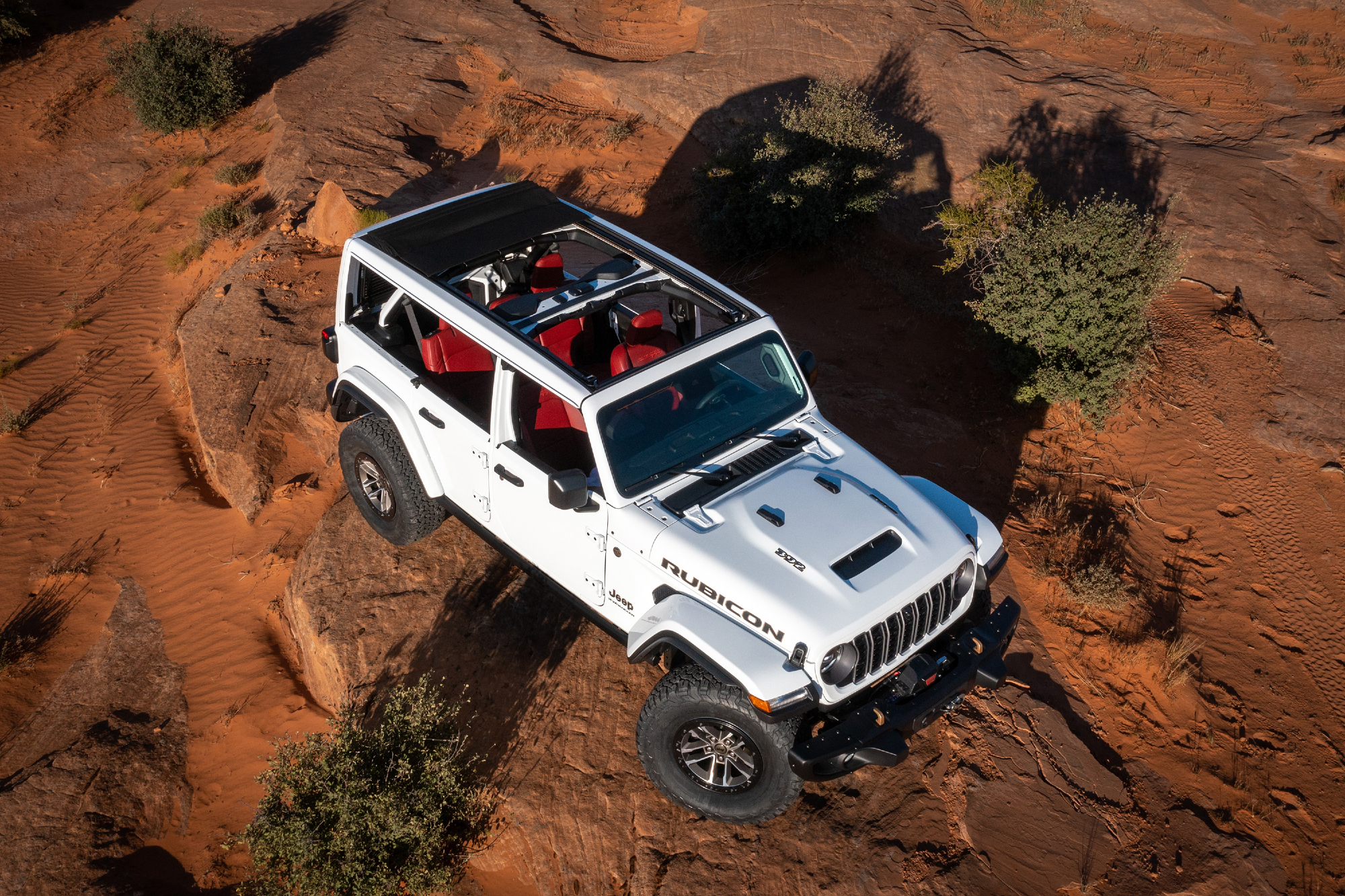 White 2024 Jeep Wranger Rubicon 392 Final Edition with roof off traveling over a rocky rise in the desert.