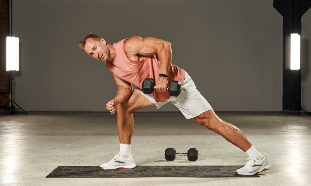 Oone-arm dumbbell row in a bent-over position with emphasis on the leg by an athlete in shorts and a T-shirt