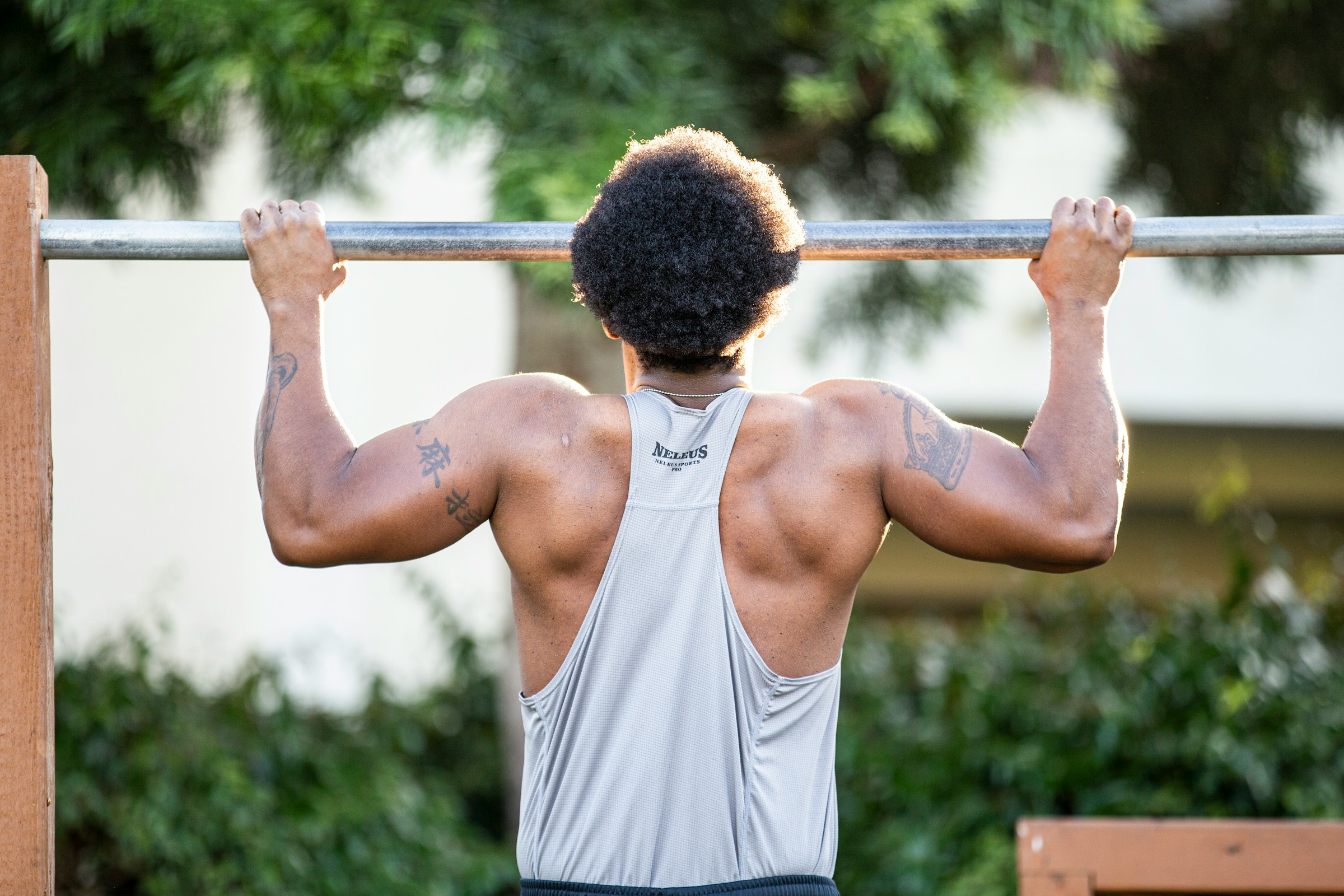 man wearing white shirt outside doing pull ups exercise on silver bar