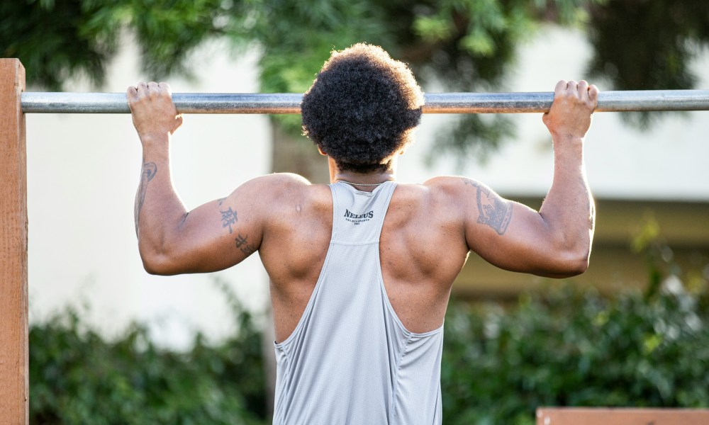 man wearing white shirt outside doing pull ups exercise on silver bar