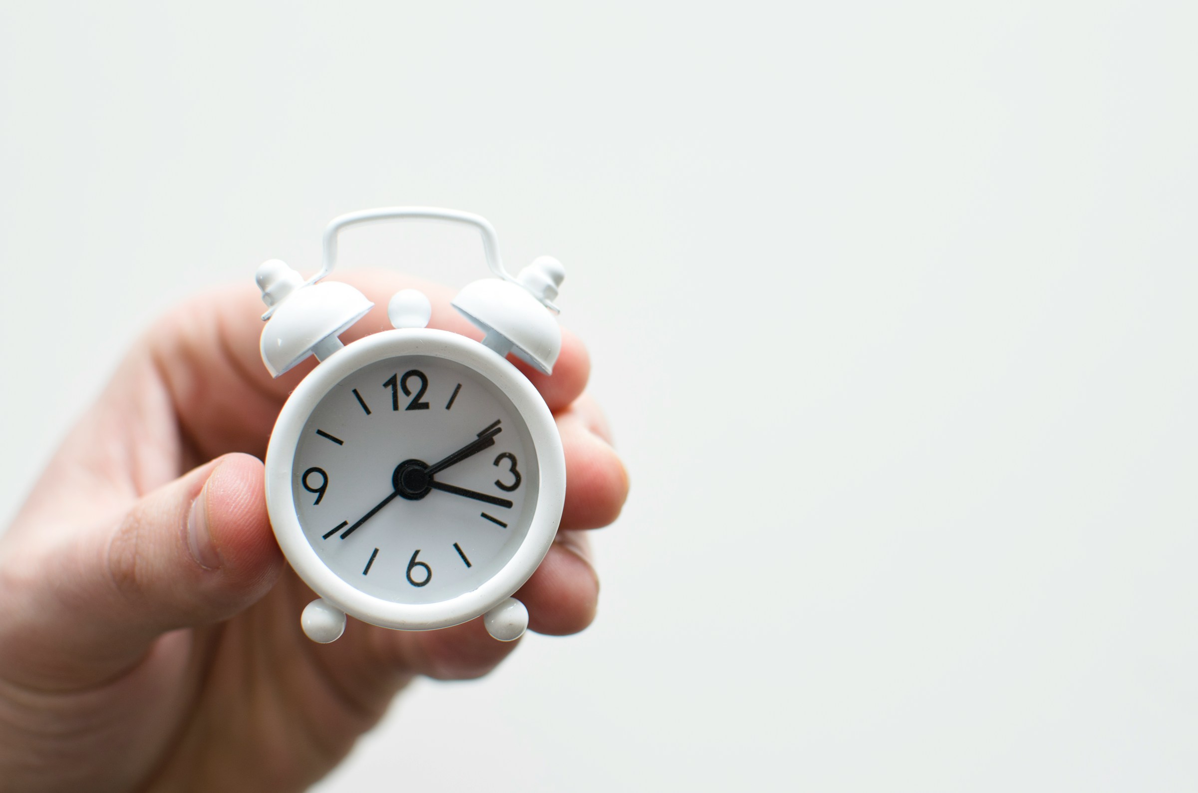 time consuming hand holding a little white clock close up