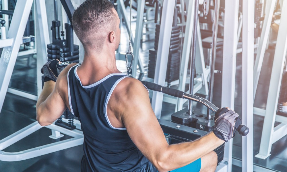 Caucasian muscular man using pull down machine in the gym, weight lifting workout.