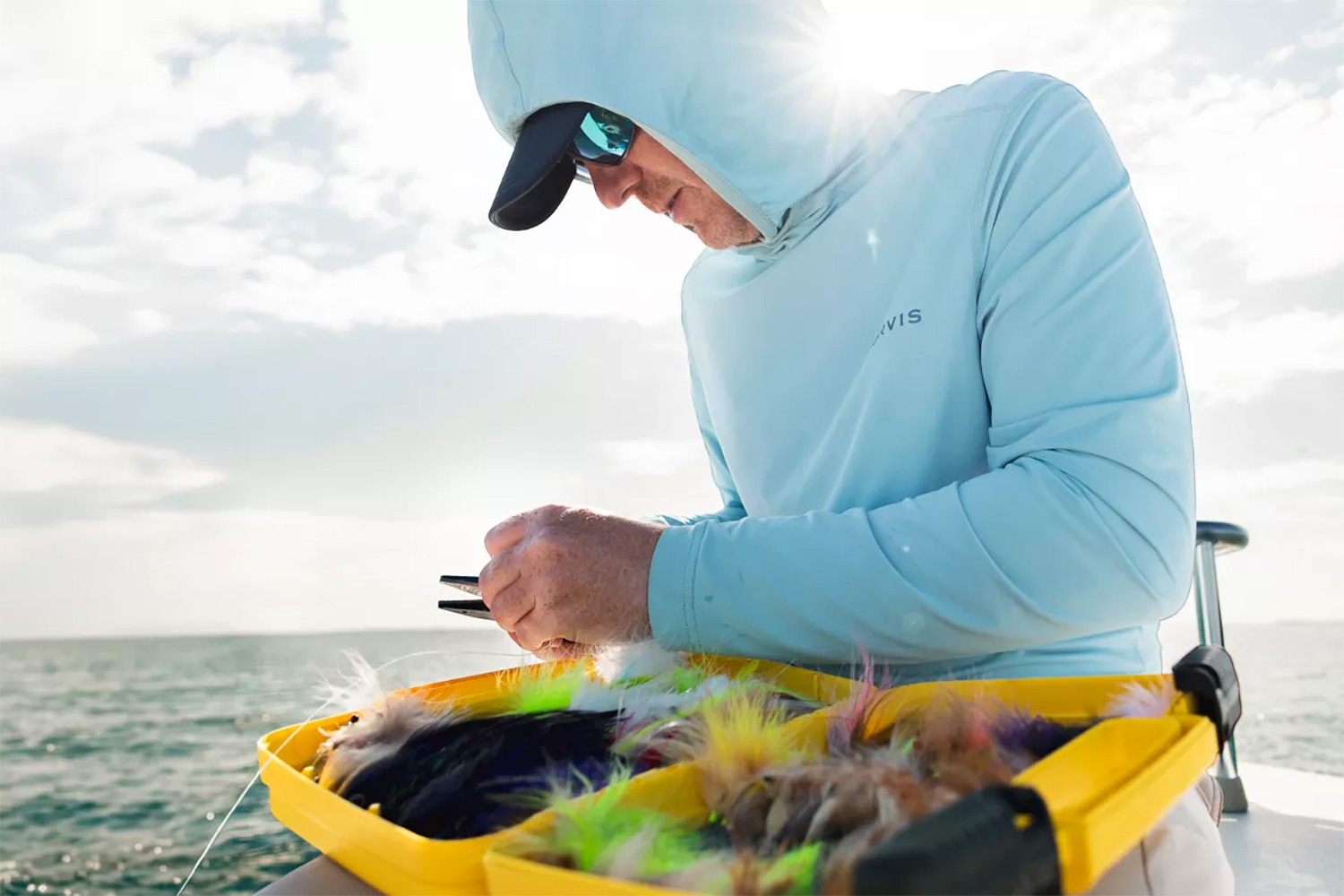 Man fishing on a boat while wearing an Orvis DriCast sun protection hoodie.