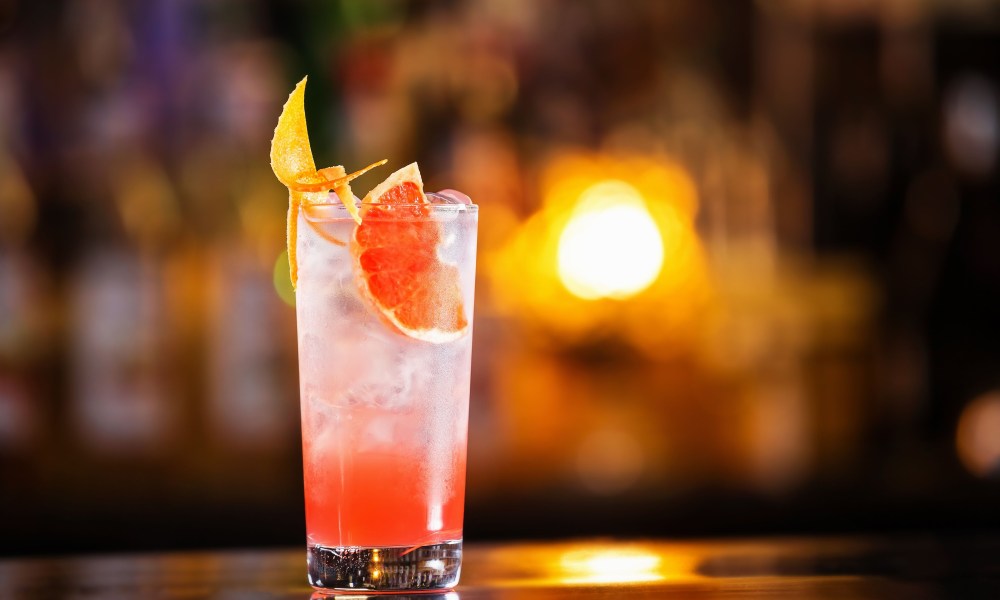 Closeup glass of greyhound cocktail decorated with grapefruit at bright bar counter background.