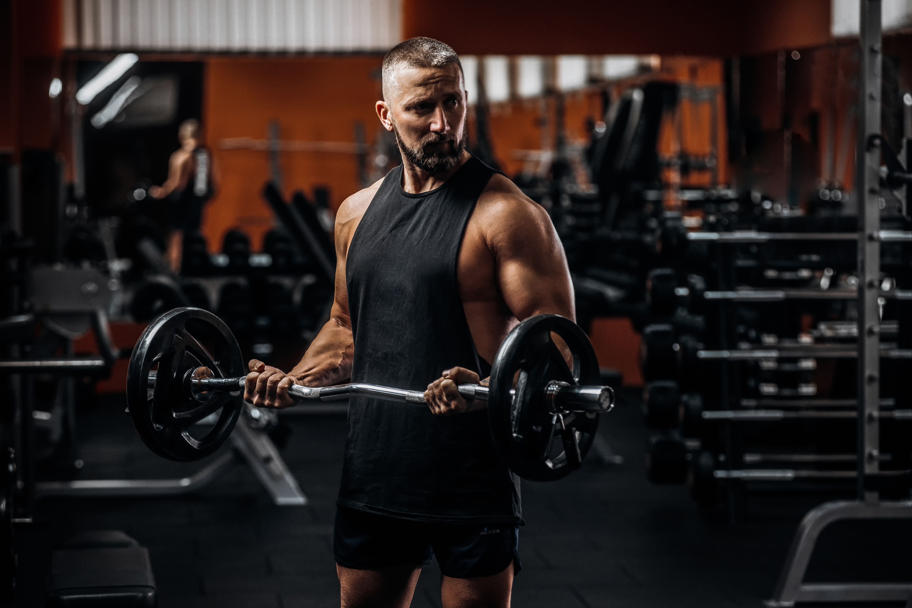 Fit strong man doing biceps curl with barbell in gym