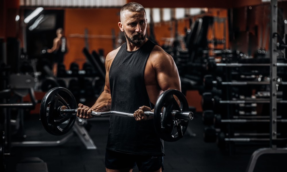 Fit strong man doing biceps curl with barbell in gym