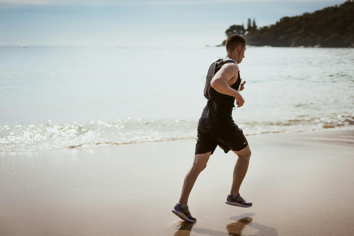 man running on beach, wide shot of his bacl