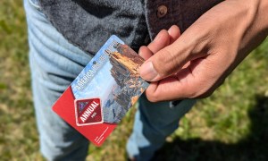 A man holding an America the beautiful parks pass wearing a button down top and blue jeans standing outdoors