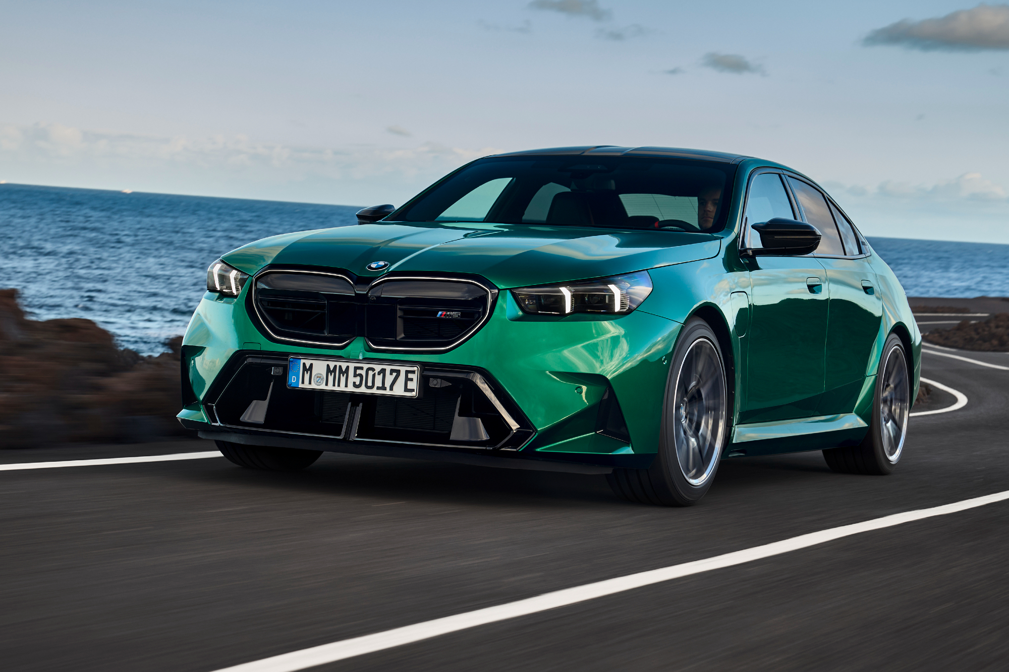 2025 BMW M5 performance design driving on a winding ocean-side paved road.