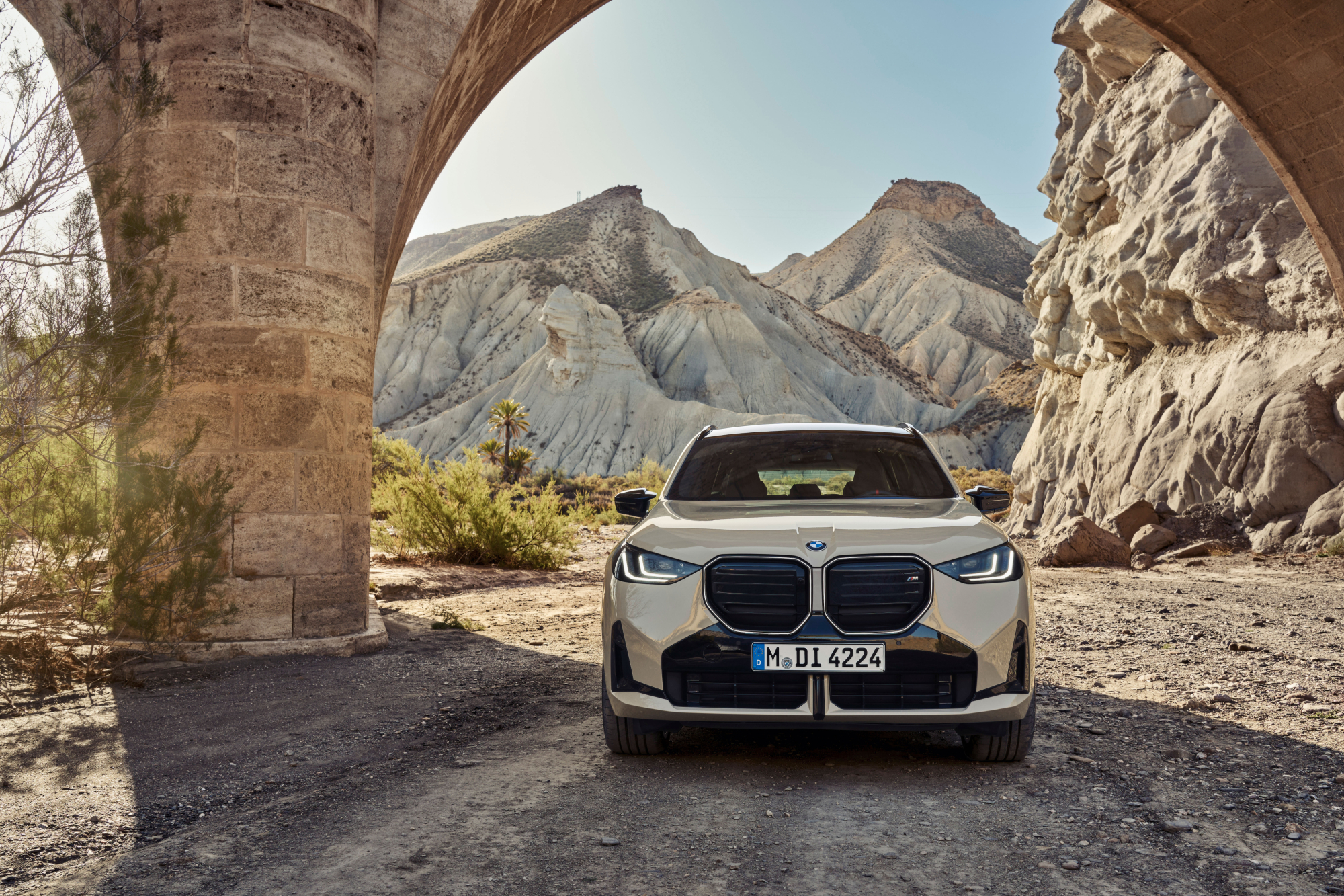2025 BMW X3 M50 xDrive direct front view with the car parked under a stone structure in the desert.