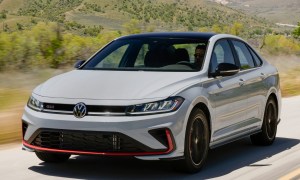 2025 VW Jetta GLI left front three-quarter view driving on a paved road in the countryside with mountains in the background.