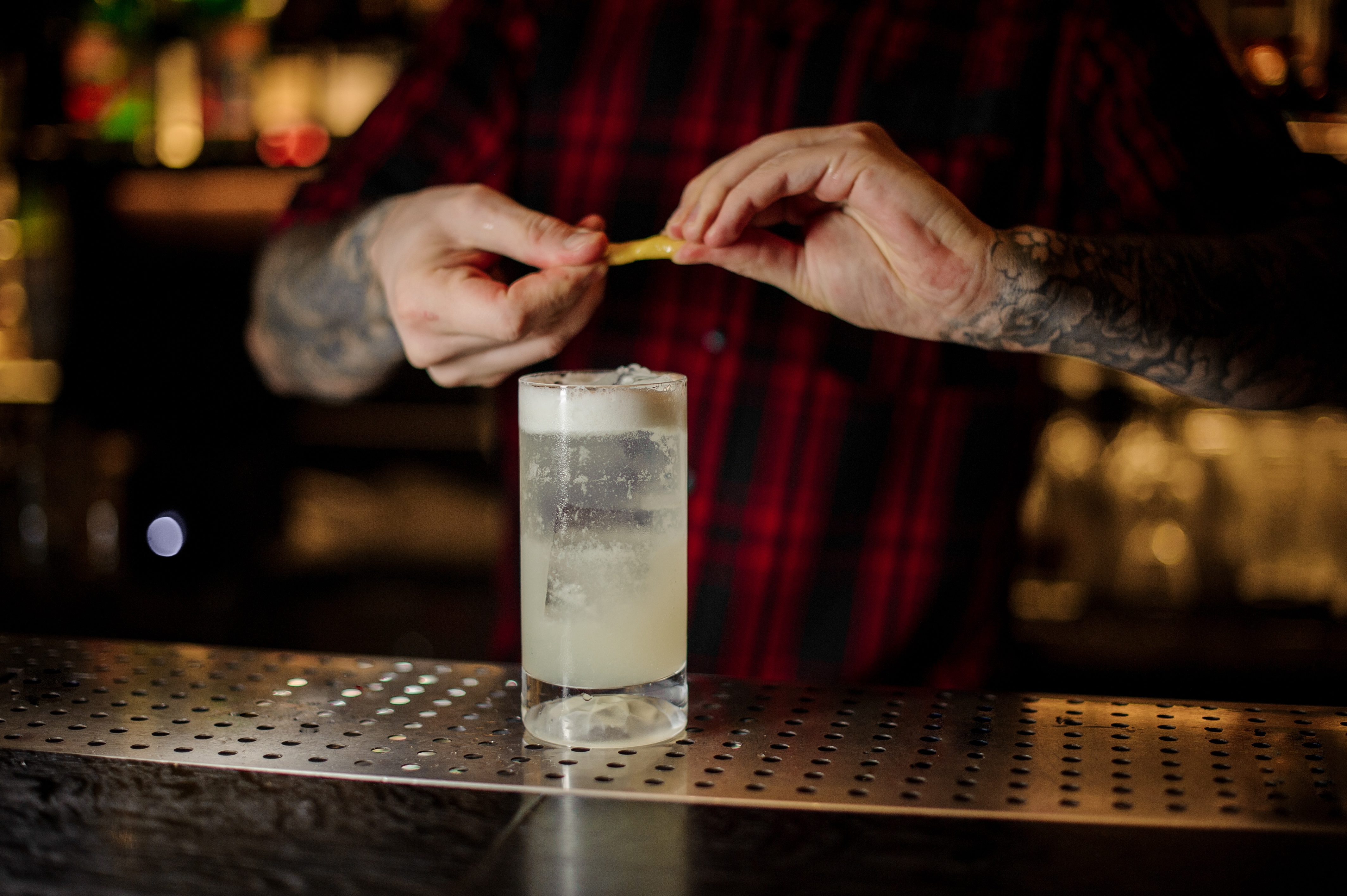 Bartender adding orange zest juice to a Gin Fizz cocktail in the glass on the bar counter