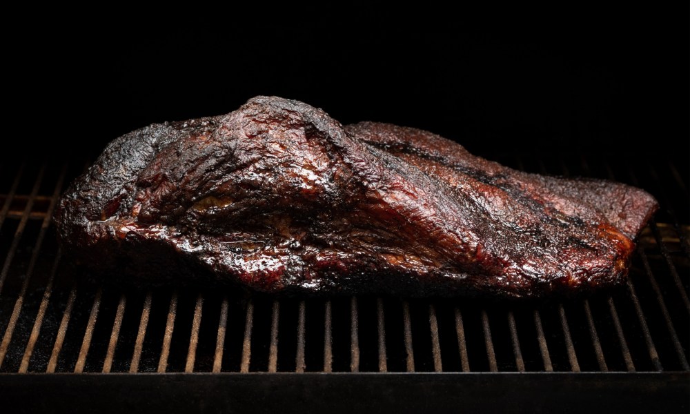 Slow cooked beef brisket on the grill grates of a smoker barbecue, in a cooking background