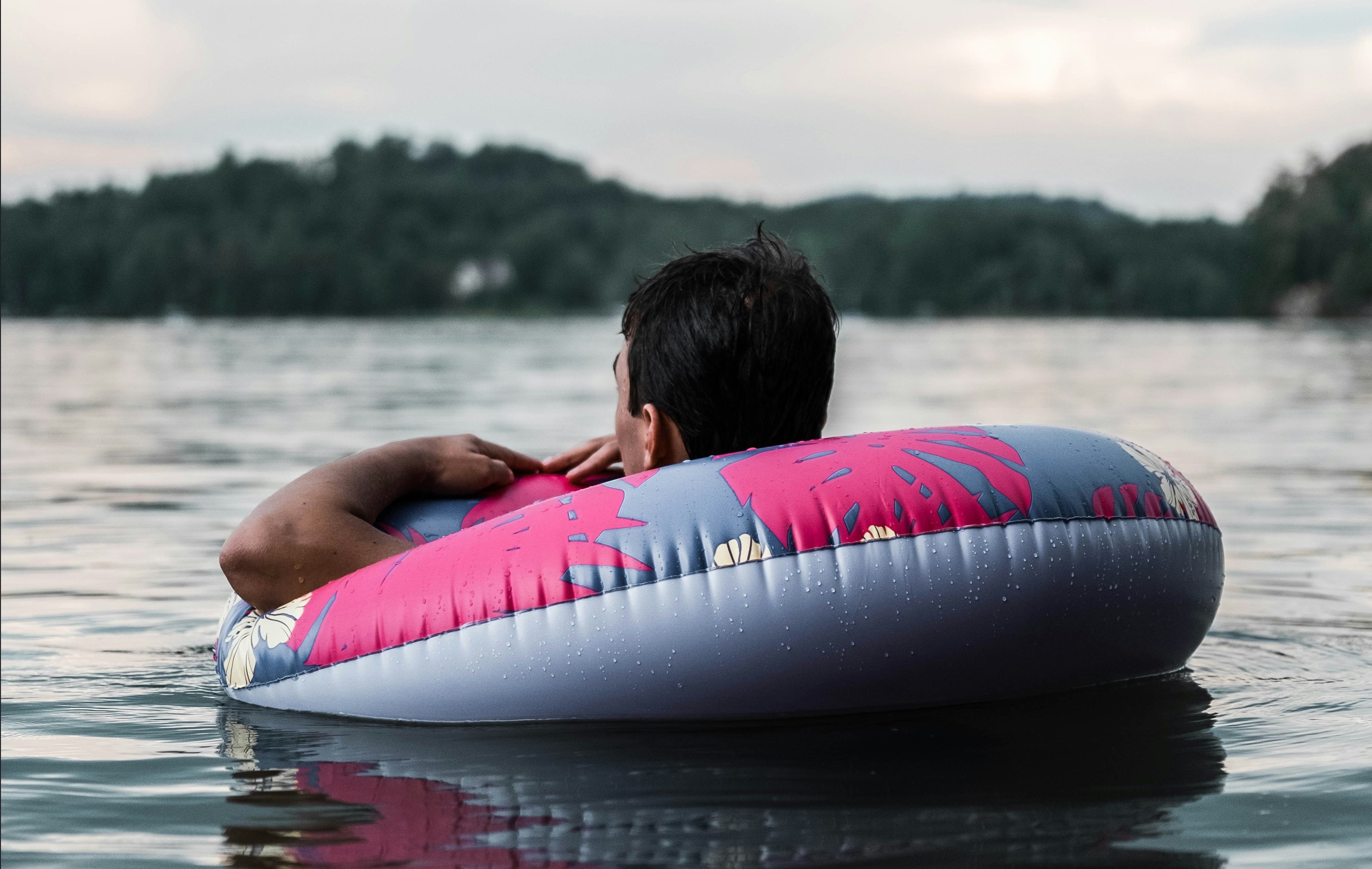 A man floating on a river in an inner tube on a cloudy day with hills in the background