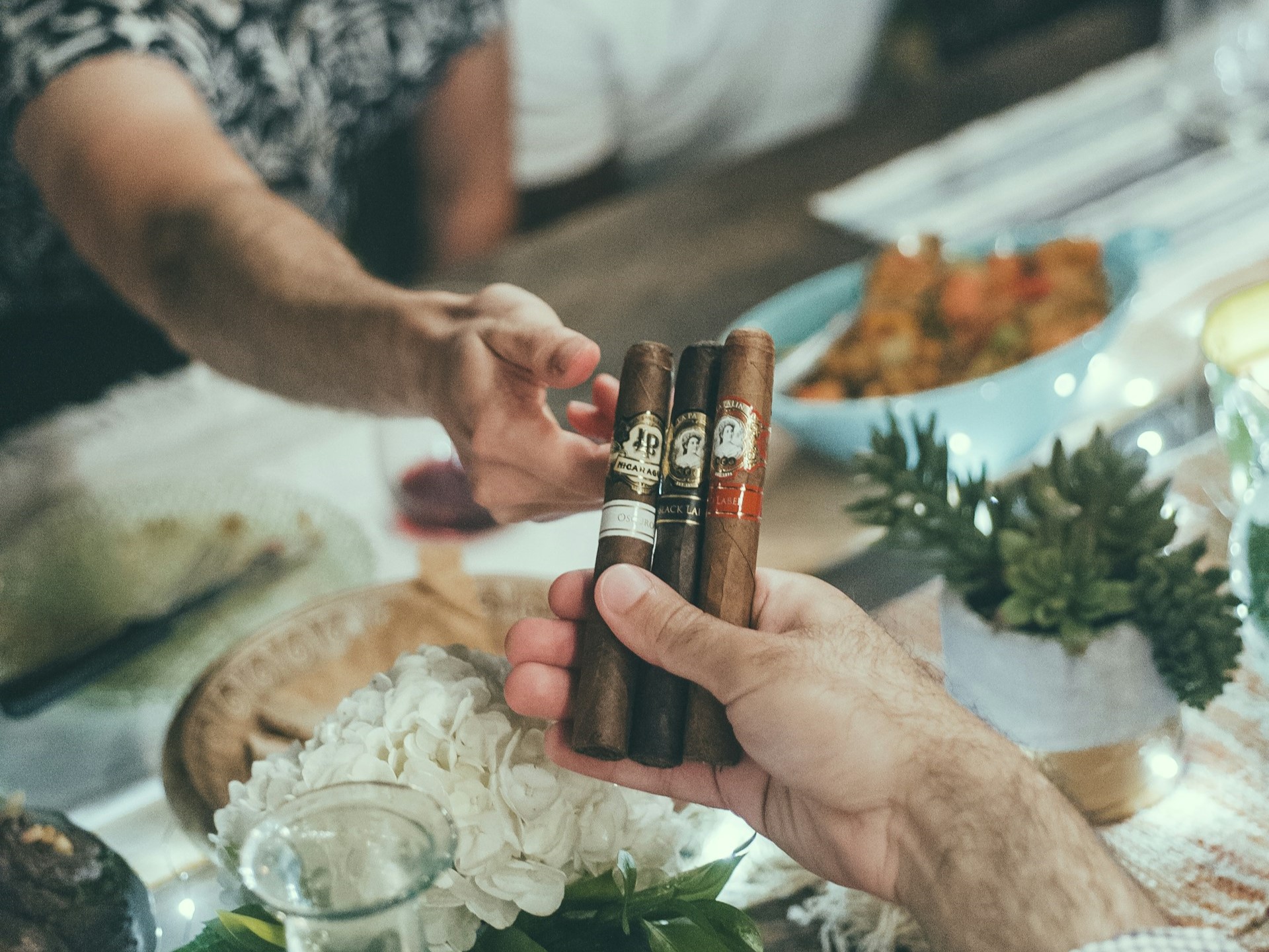 Man passes a few La Palina cigars to a friend across the dining table.