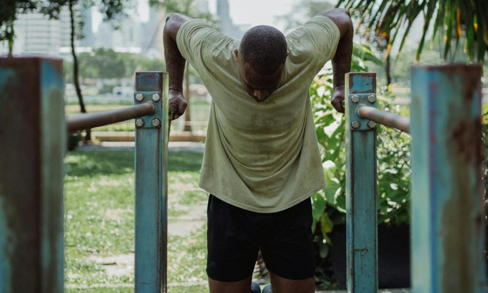 Man wearing a T-shirt and shorts doing dips exercise on metal bars outside