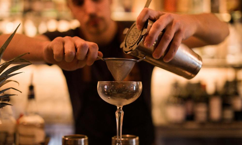 Bartender pouring drink through strainer