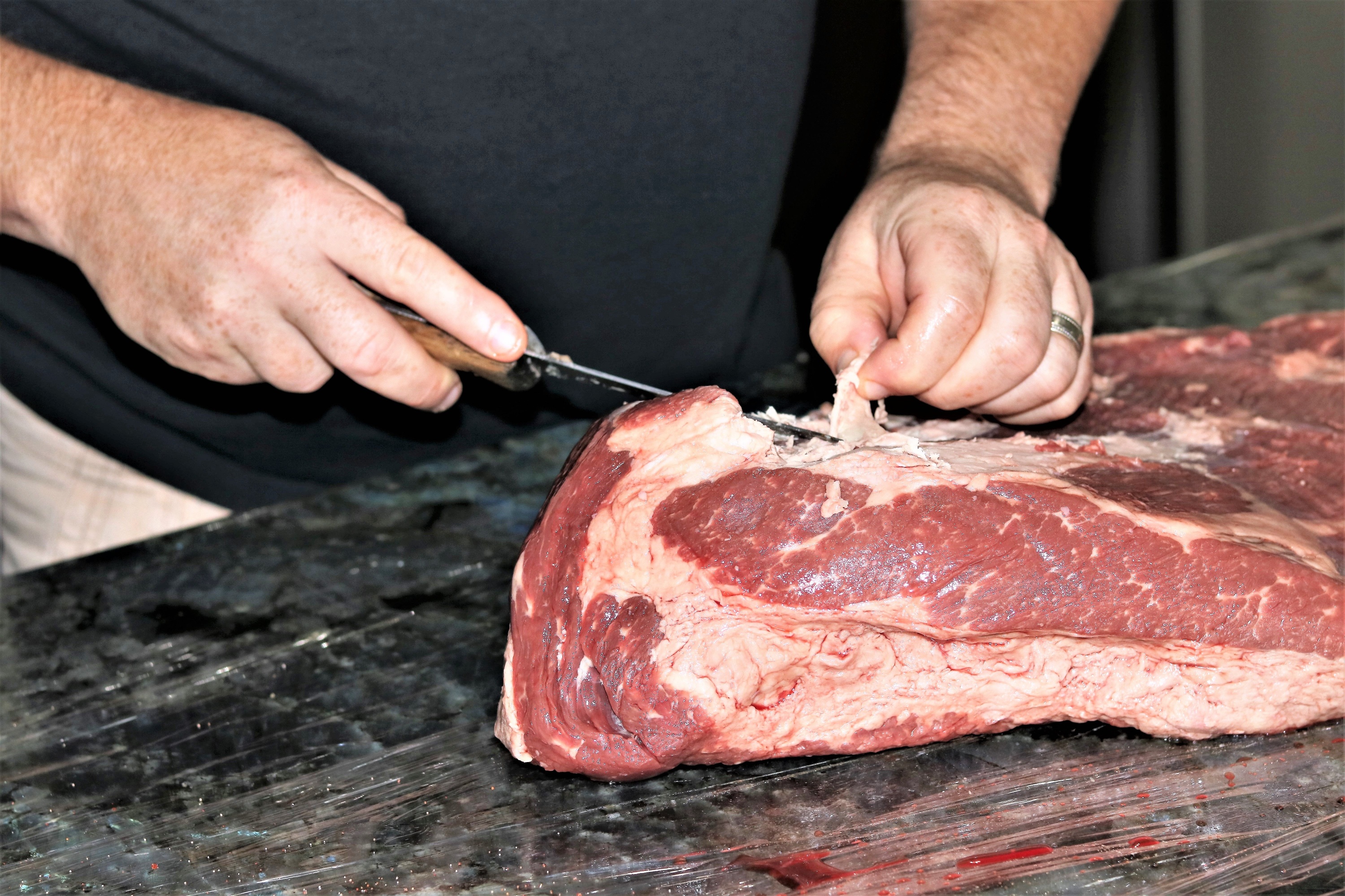 Pieces of fat being carefully trimmed from a fresh beef brisket.