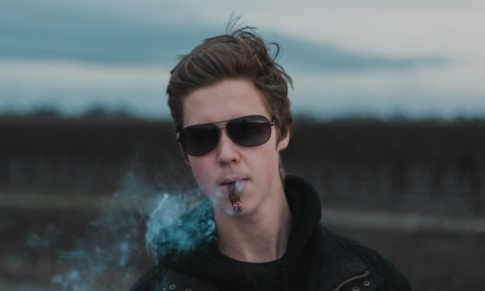 Young man enjoying a cigar outside on a gloomy day.