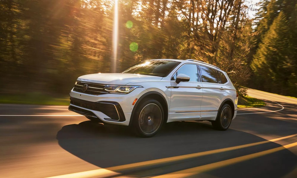 2024 VW Tiguan in Pure White driving on a curved road through a forested area.