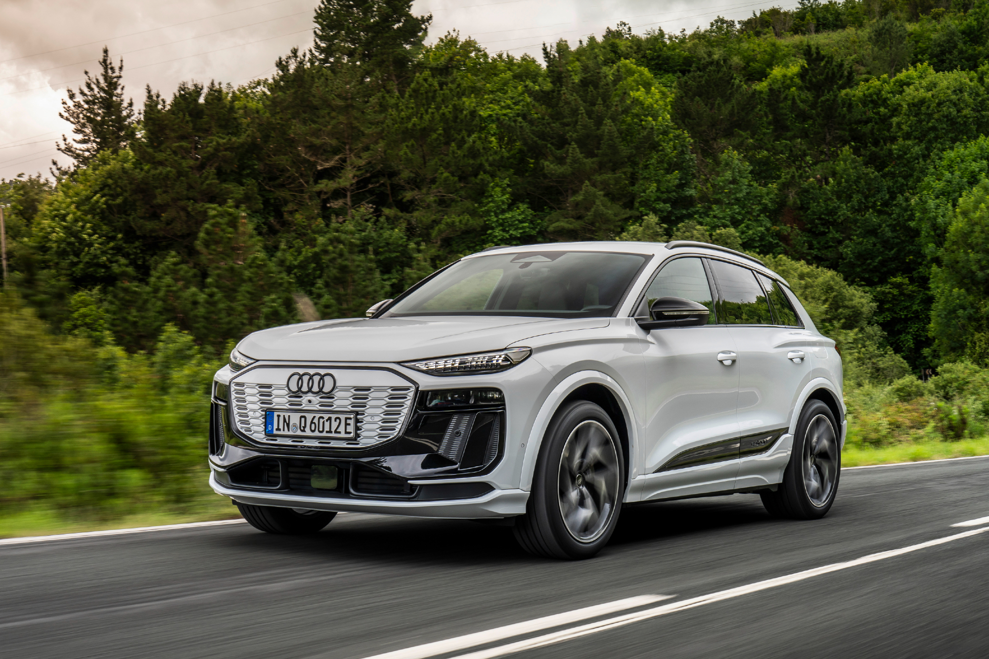2025 Audi Q6 e-tron European model driving on a highway with forest in the background.
