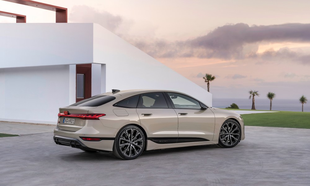 2025 Audi e-tron Sportback right side view parked beside a house with a lawn and ocean in the background.