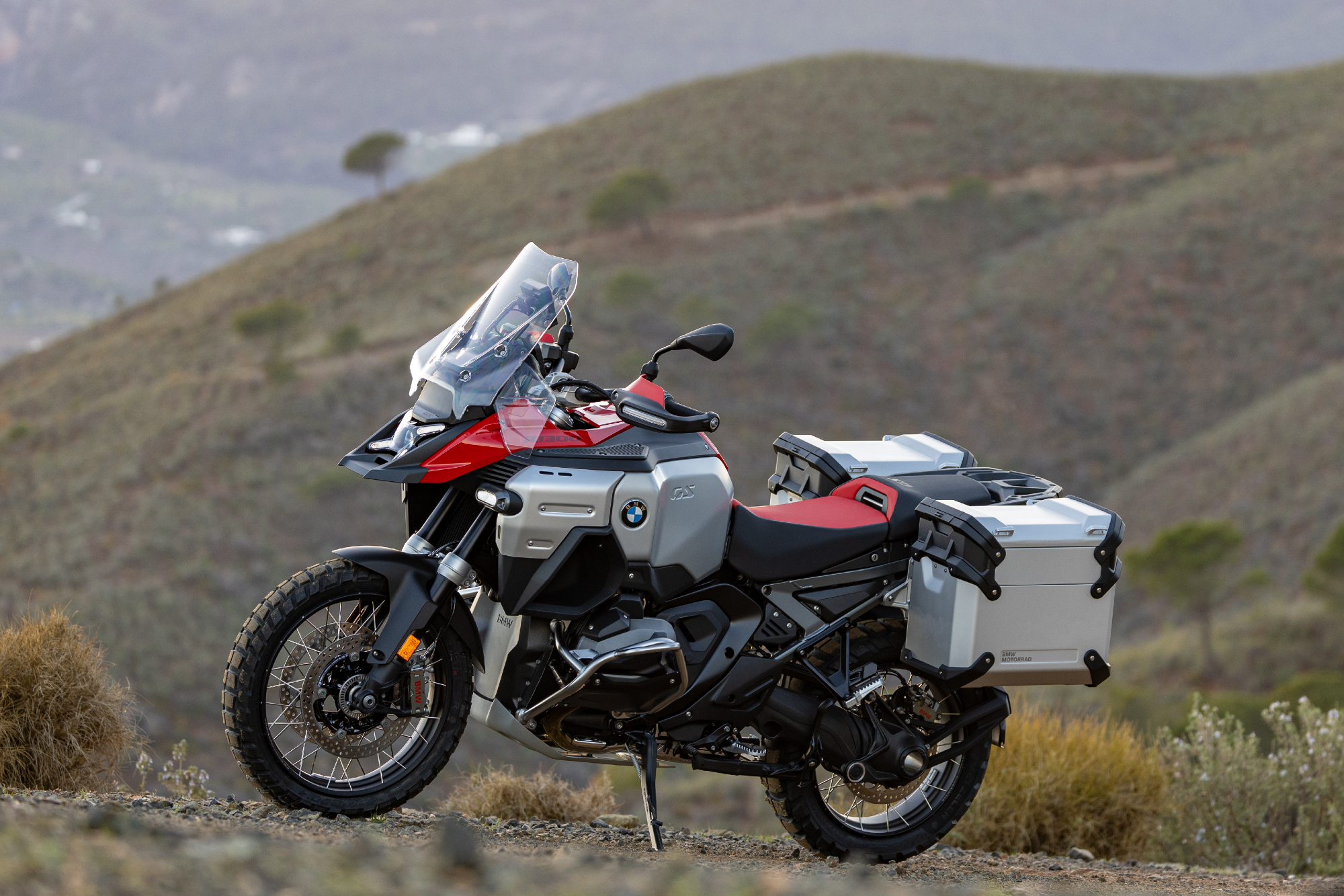 2025 BMW R 1300 GS Adventure parked on a hillside with mountains in the background.