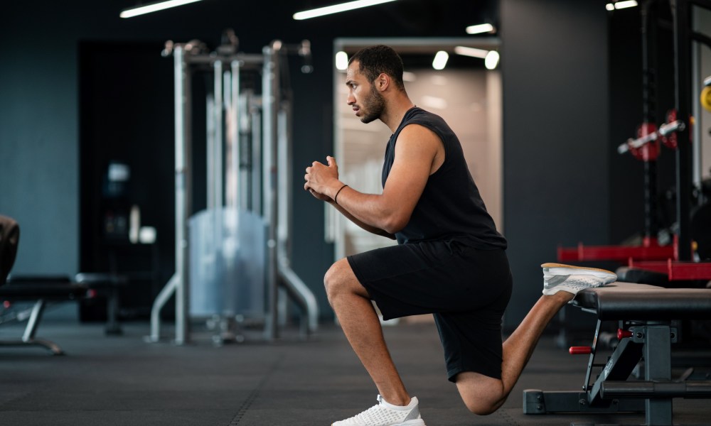 Man in gym with shorts doing Bulgarian split squat exercise in gym