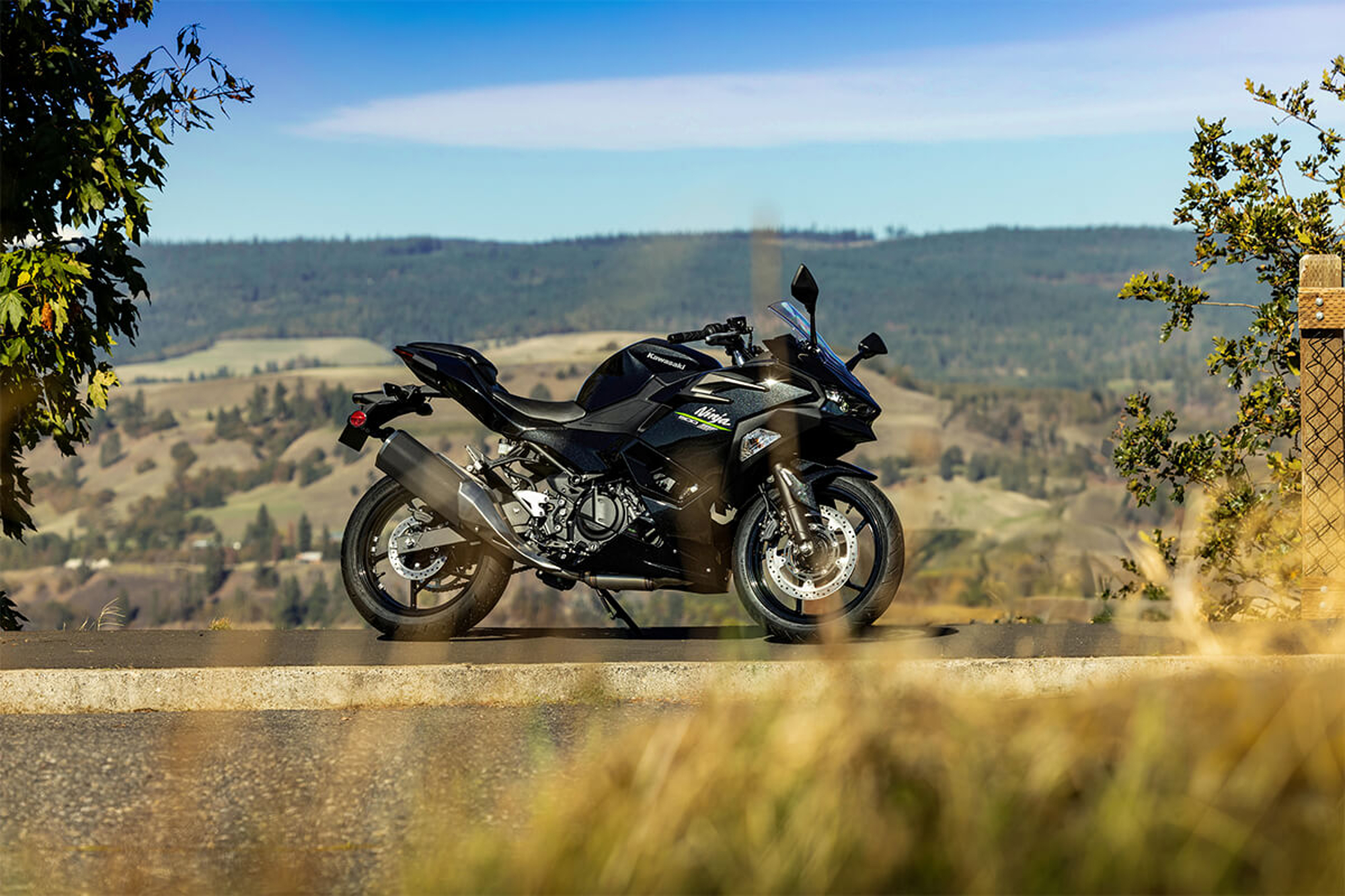 Black 2024 Kawasaki 500 parked on the side of the road with rolling hills in the background.