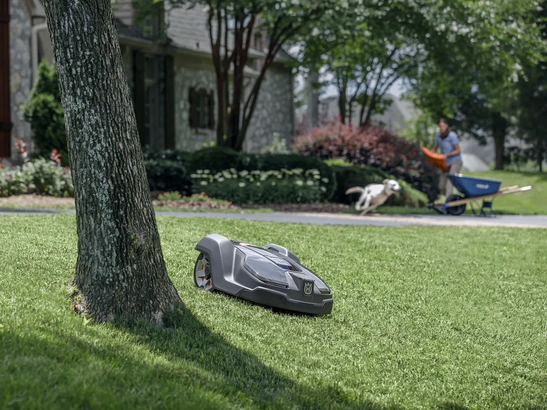 Husqvarna Automower 430XH mowing while someone does yardwork in the background