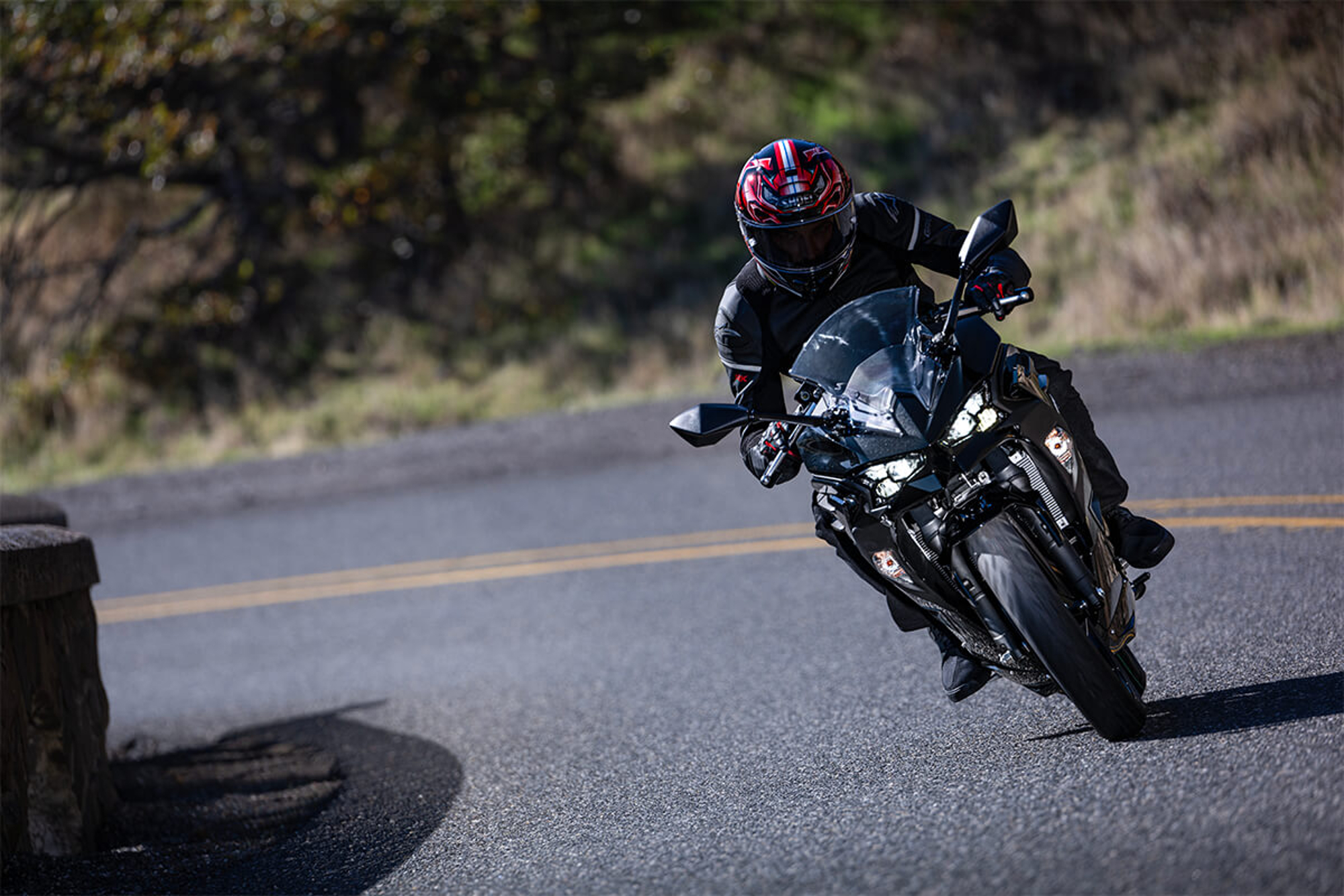 Rider on a black 2024 Kawasaki 500 on a curve on a road through mountains coming straight at the camera.