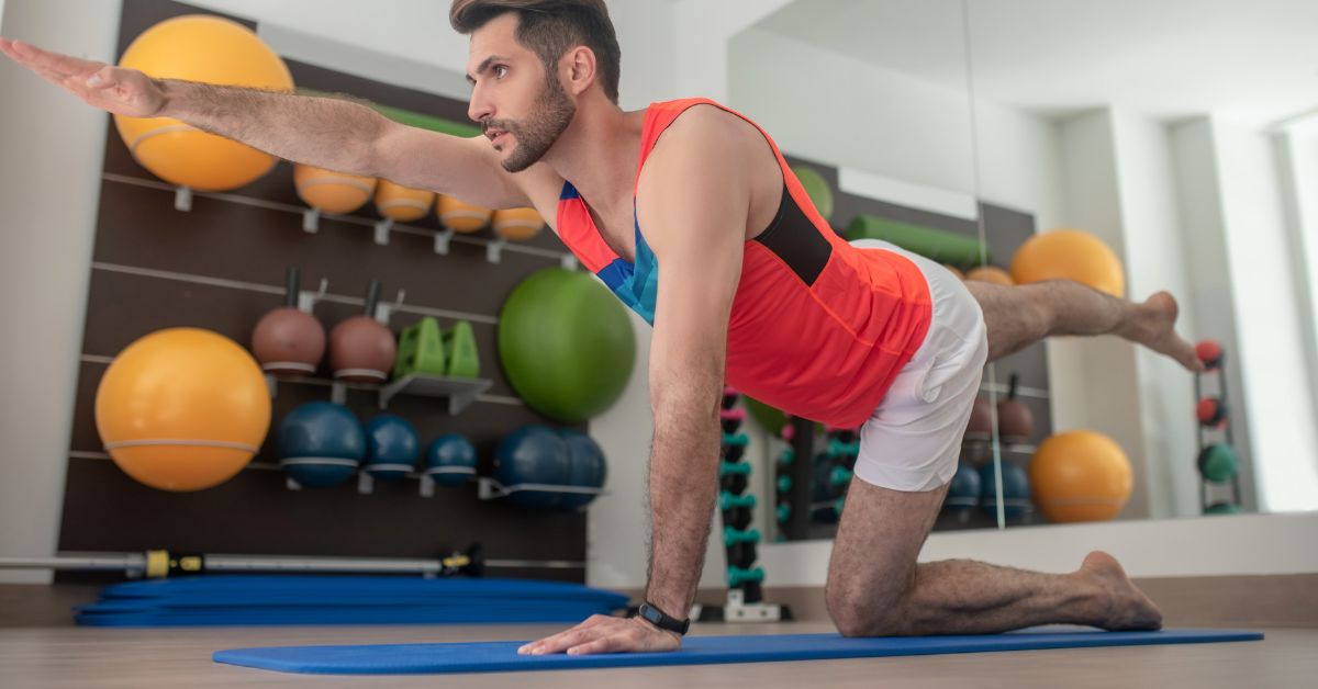 man in red doing bird dog exercise on blue mat