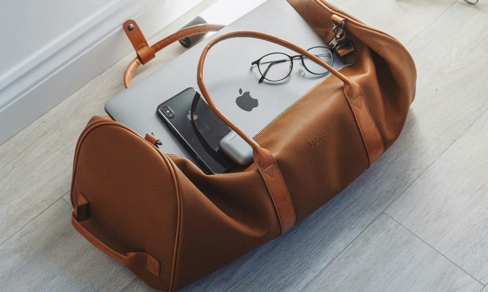 laptop and phone sit in an open brown duffel bag on the floor