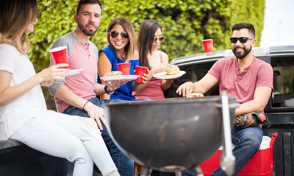 Group of friends laughing and eating while tailgating.