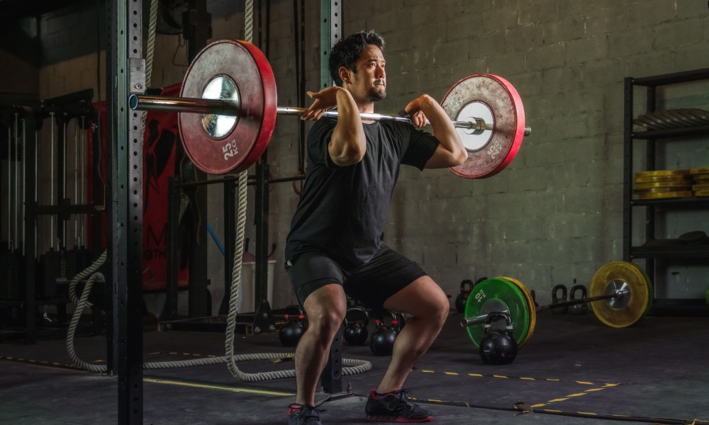 Athletic man having workout and bodybuilding with barbells weight front squat setting style in gym and fitness club in dark tone