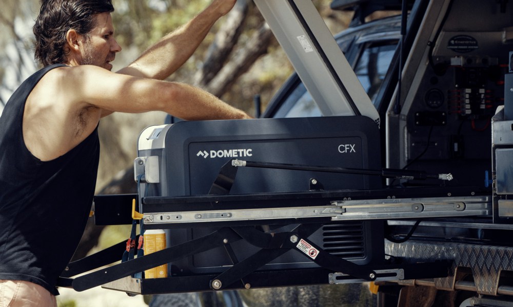 Man opening a Dometic portable refrigerator mounted inside a truck.