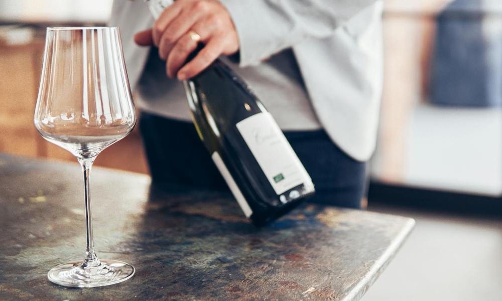 Person opening wine bottle with empty wine glass