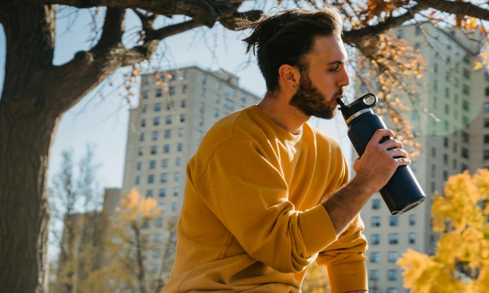 man in a yellow shirt sitting outside sipping his water bottle