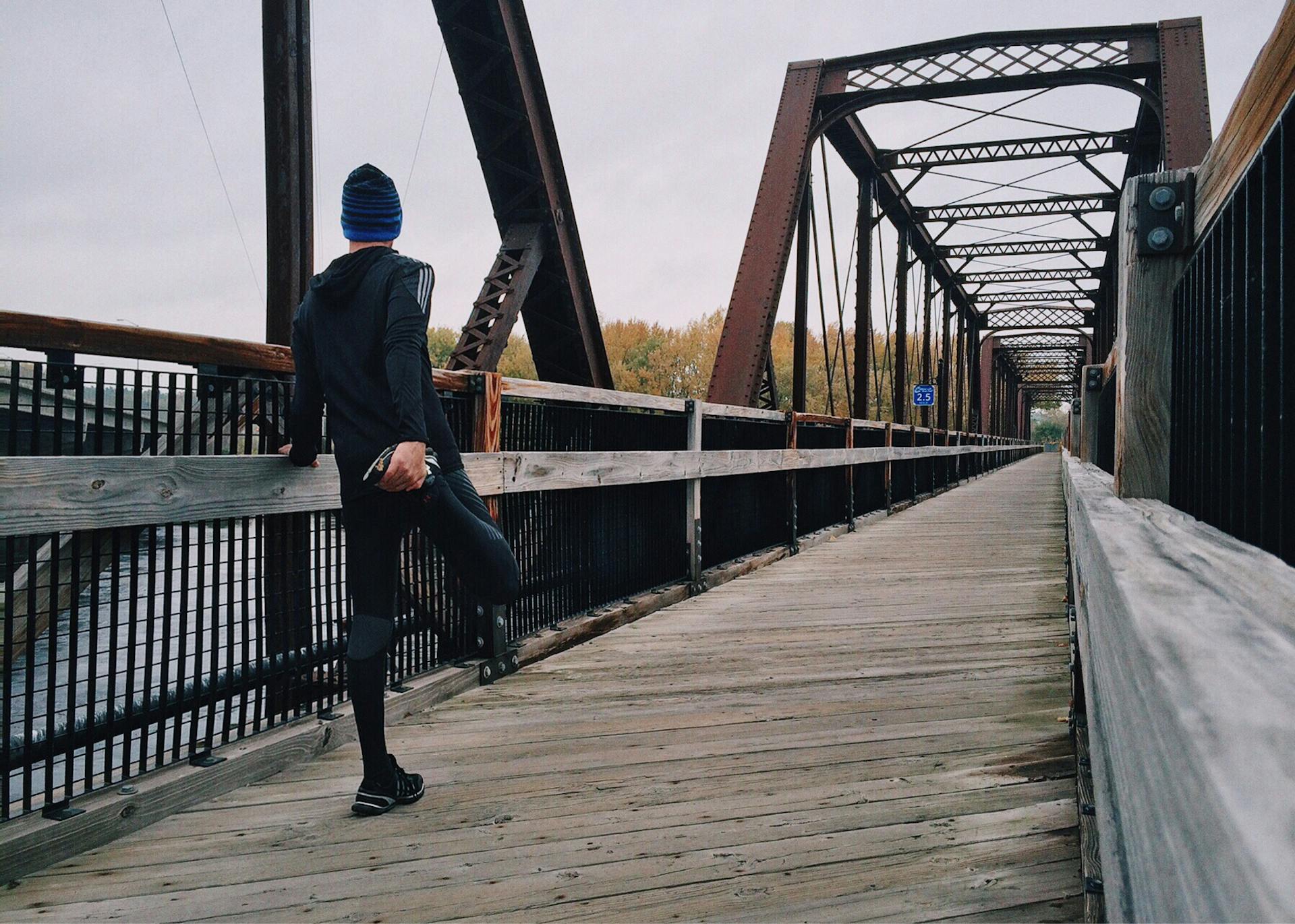 Man stretching his right hamstring on a bridge, facing away from the camera