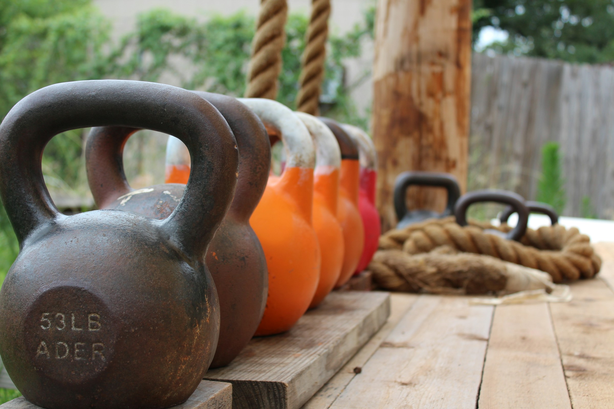 Line of kettlebells on wooden deck outside next to ropes