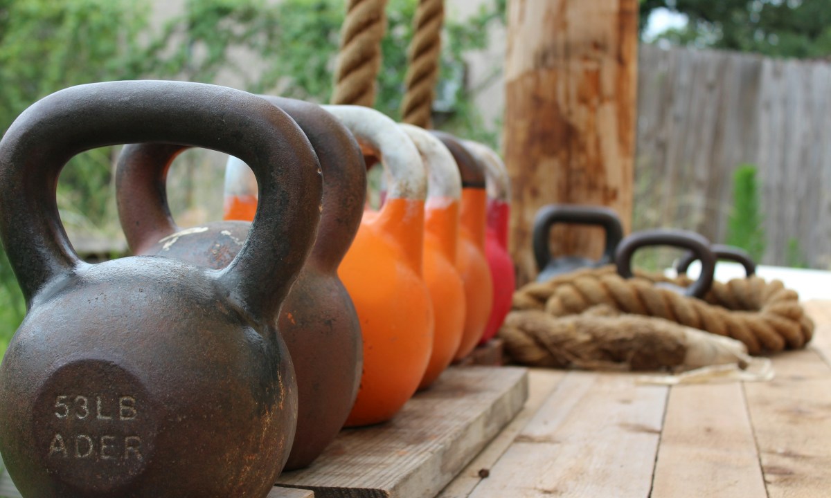 Line of kettlebells on wooden deck outside next to ropes