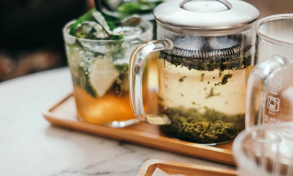 A pot of tea with a cup brewing on a tray.