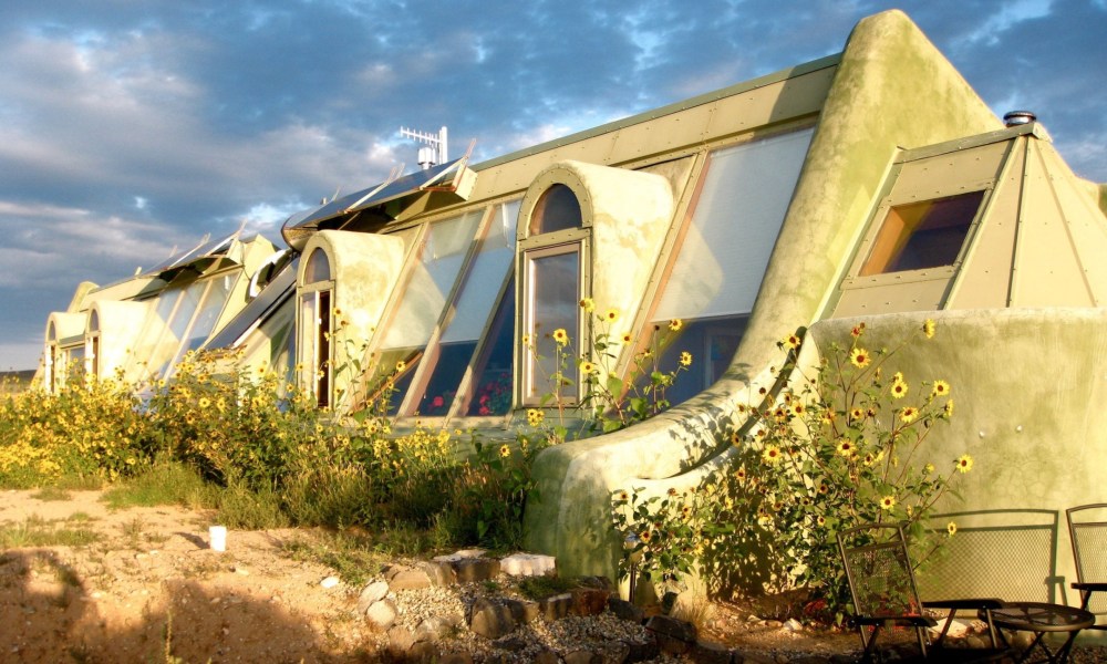 A yellow Earthship with large sloping windows