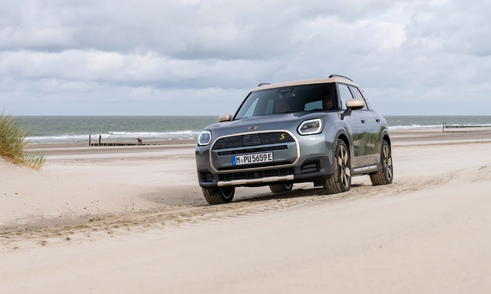 2025 all-electric MINI Countryman ALL4 SE driving on the beach away from the water coming between sand dunes.