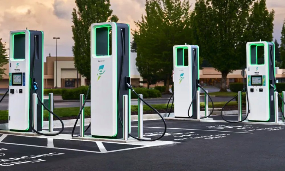 Four Electrify America charging stations in a retail shopping parking lot.