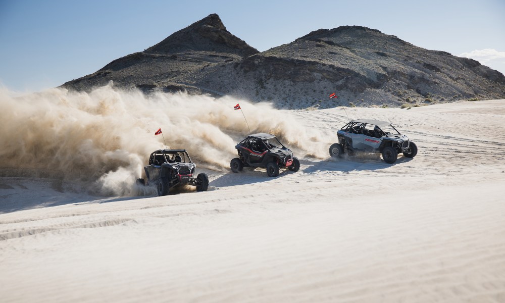 Polaris OVR 2025 RZR Pro models racing down a sand hill in the desert.