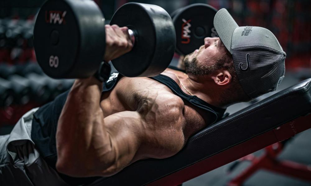 Man laying on workout bench chest pressing dumbbells hat