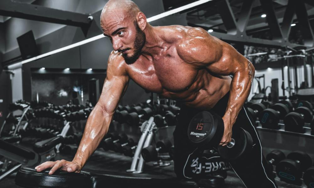 Man with shirt off in gym lifting one dumbbell