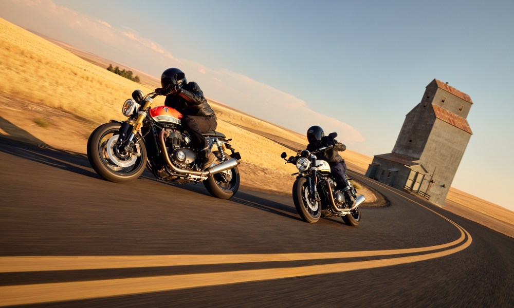 2025 Triumph Speed Twin 1200 and Speed Twin 1200 RS tucked in riding on a curved road through farm land.